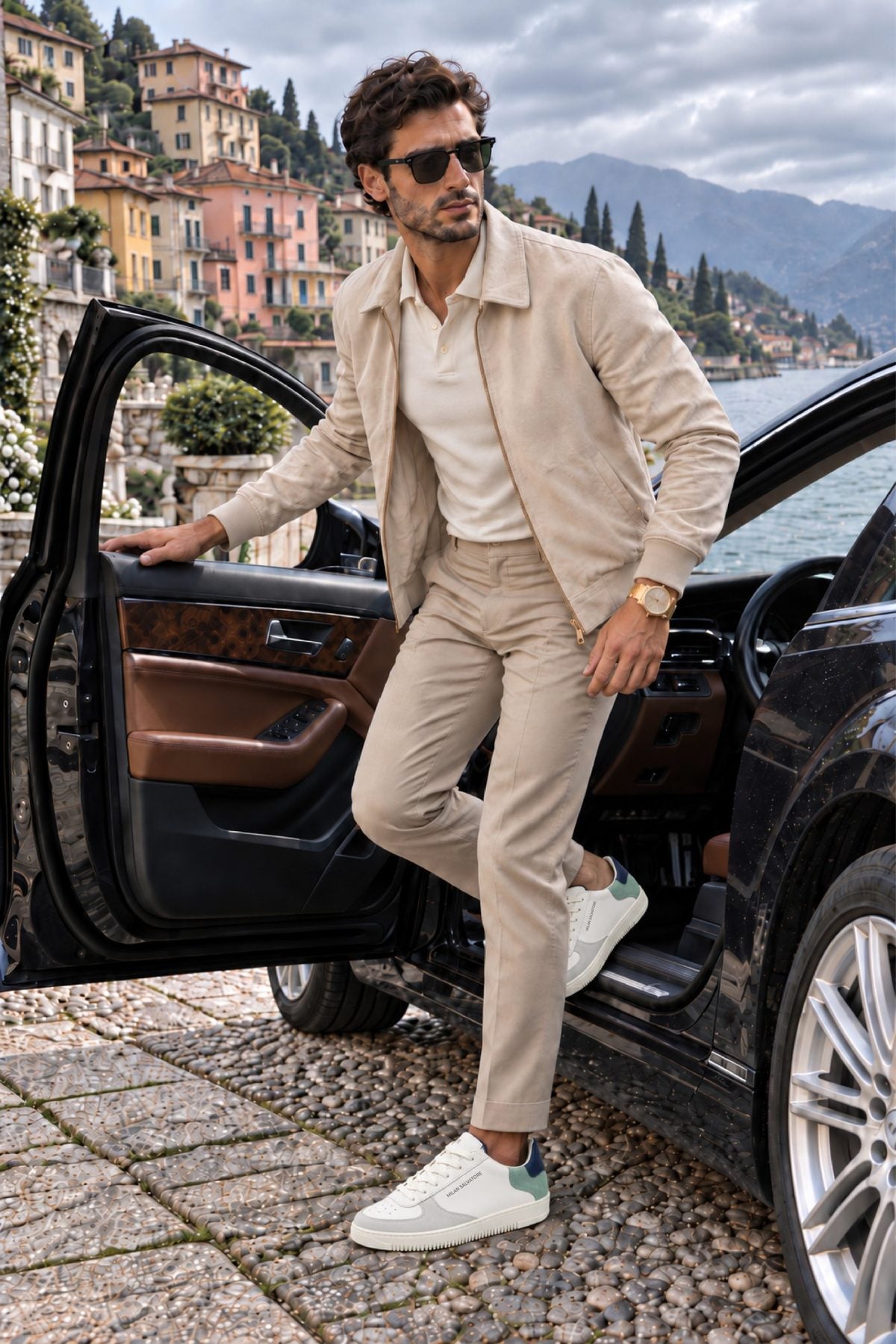 A man in a cream suede jacket and trousers stepping out of a car on Lake Como, wearing the Acquamarina Bold