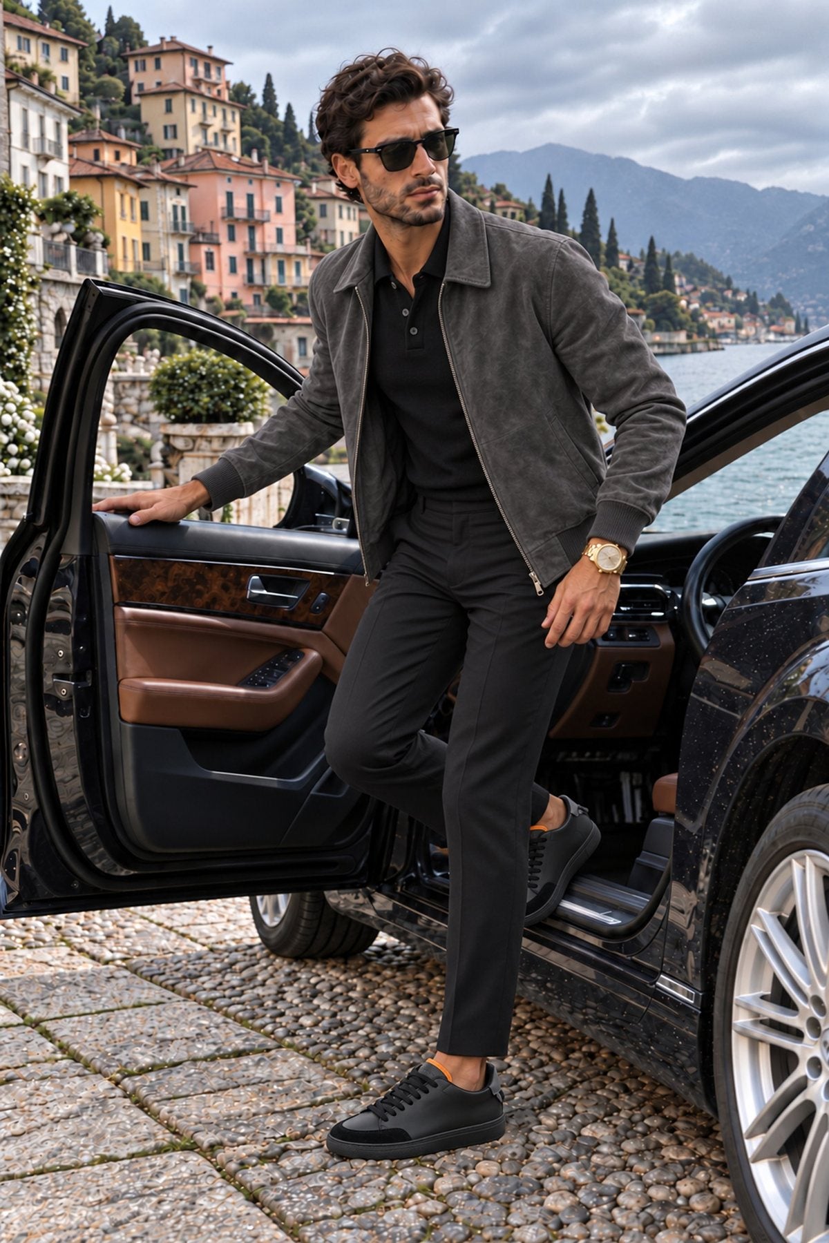 A man in a charcoal suede jacket and black trousers stepping out of a car on Lake Como, wearing the Nero Everyday