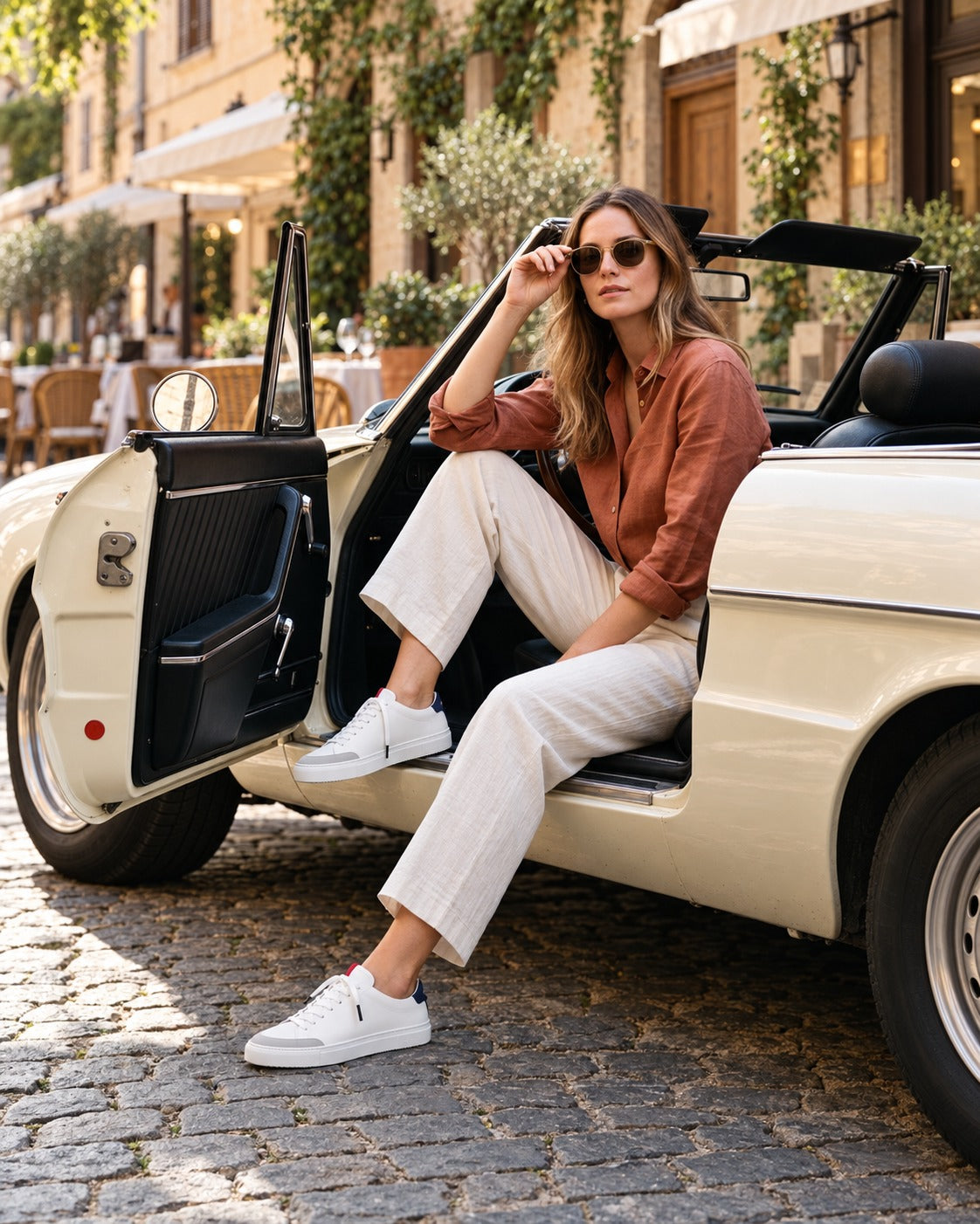 A woman in a terracotta linen shirt and cream trousers stepping out of a vintage convertible, wearing the Patriot Everyday