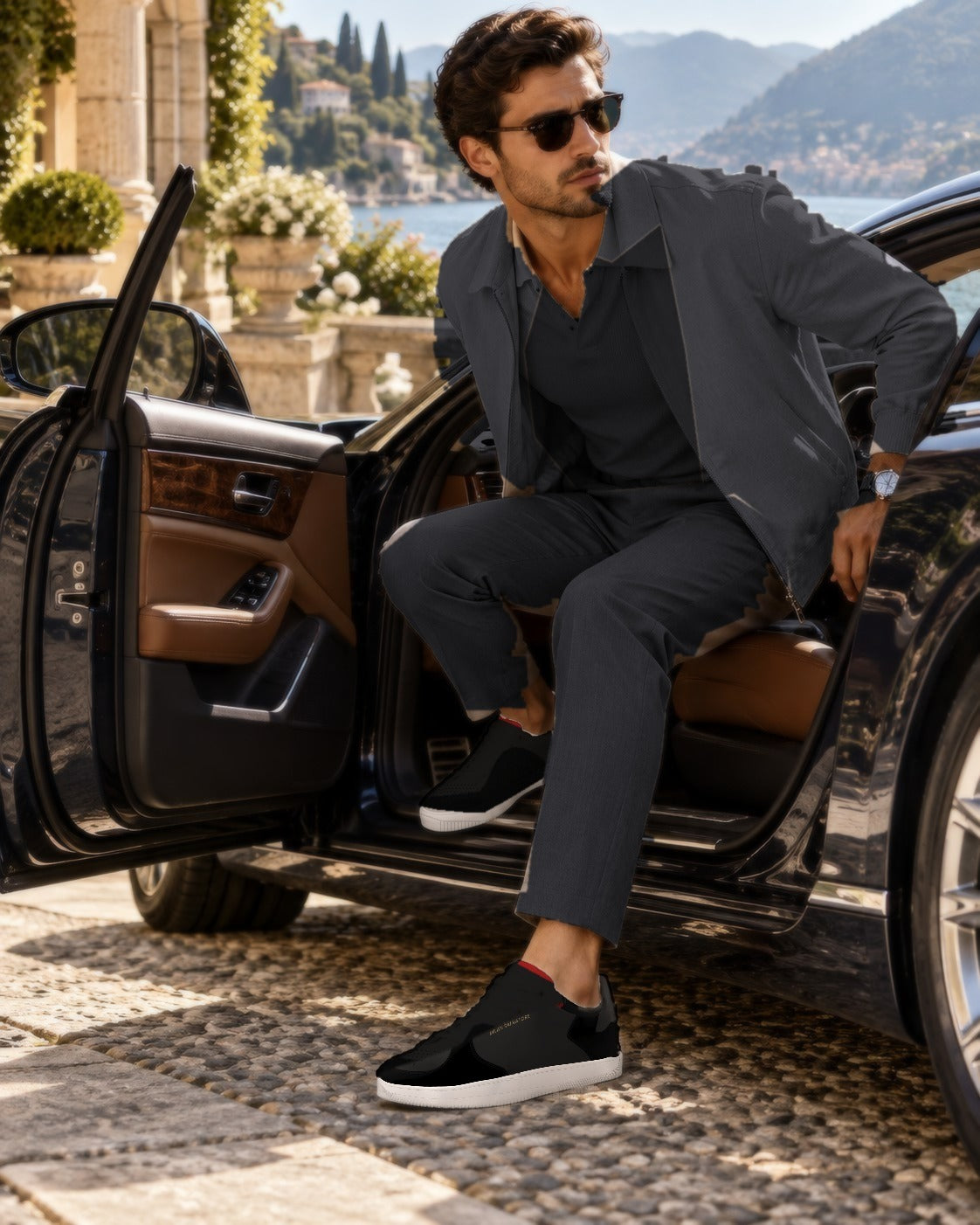 A man in a charcoal jacket and trousers stepping out of a car on the Italian lakes, wearing the Nero Bold